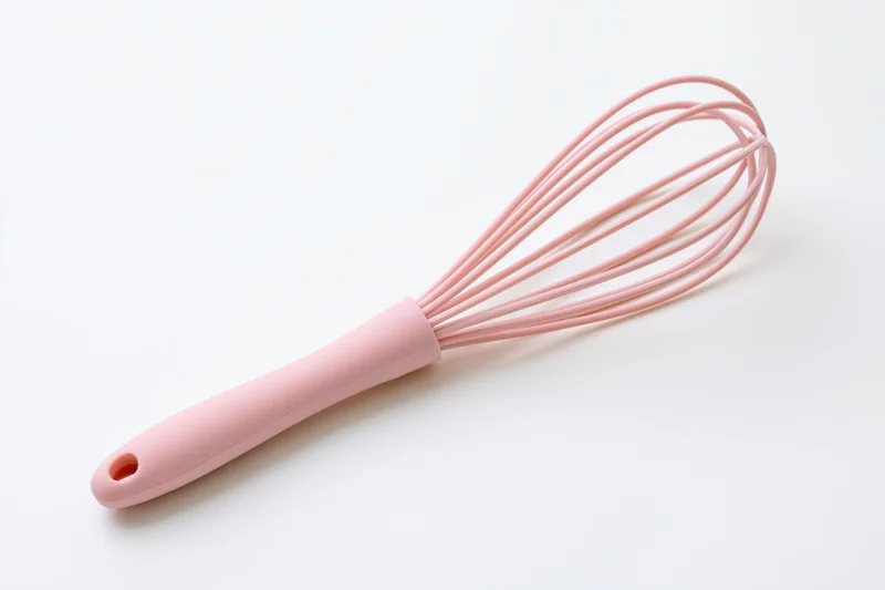 Pink silicone balloon whisk lying diagonally on white background