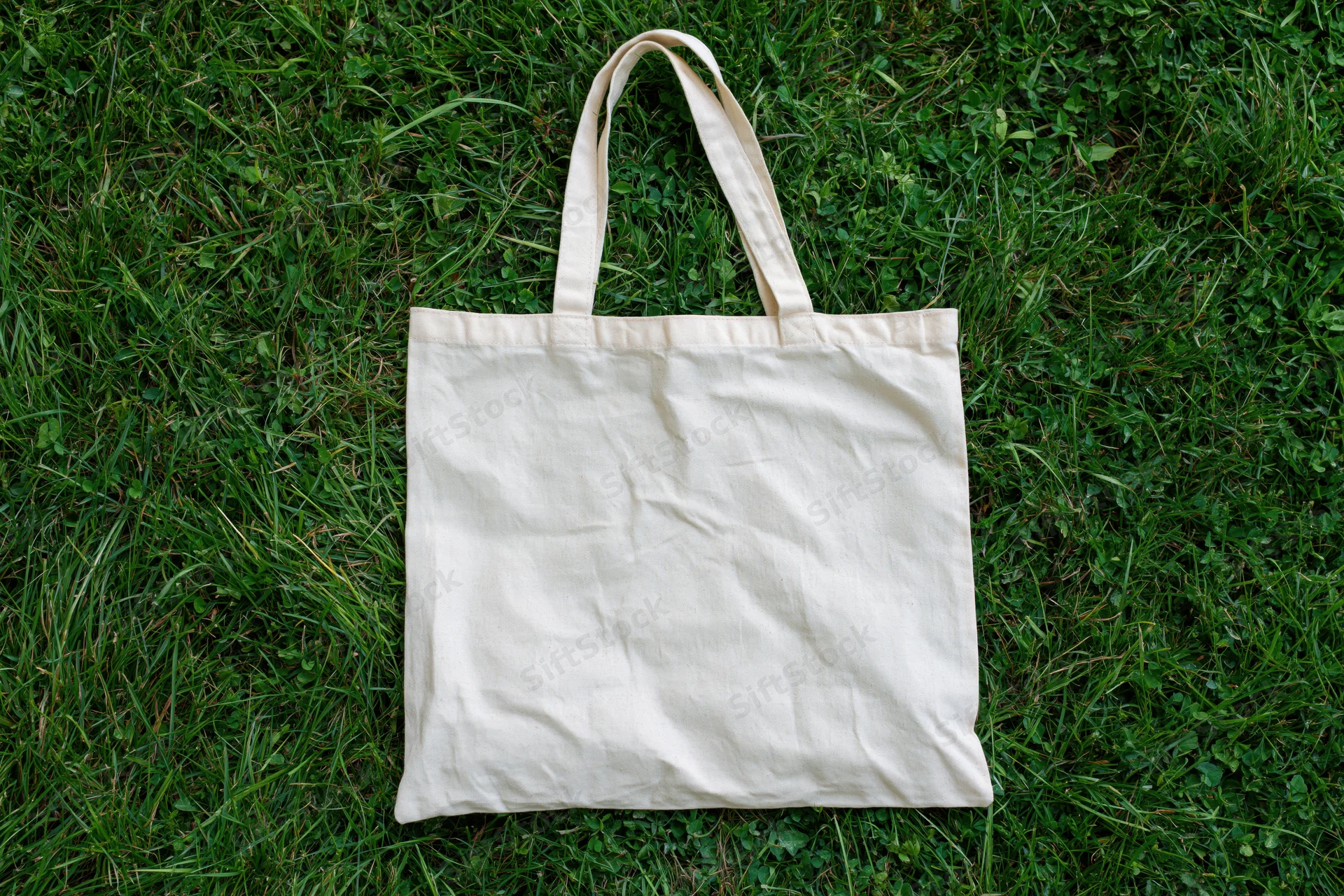Off-white canvas tote bag lying flat on green grass outdoors
