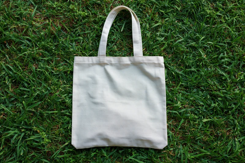 Off-white canvas tote bag lying flat on green grass outdoors