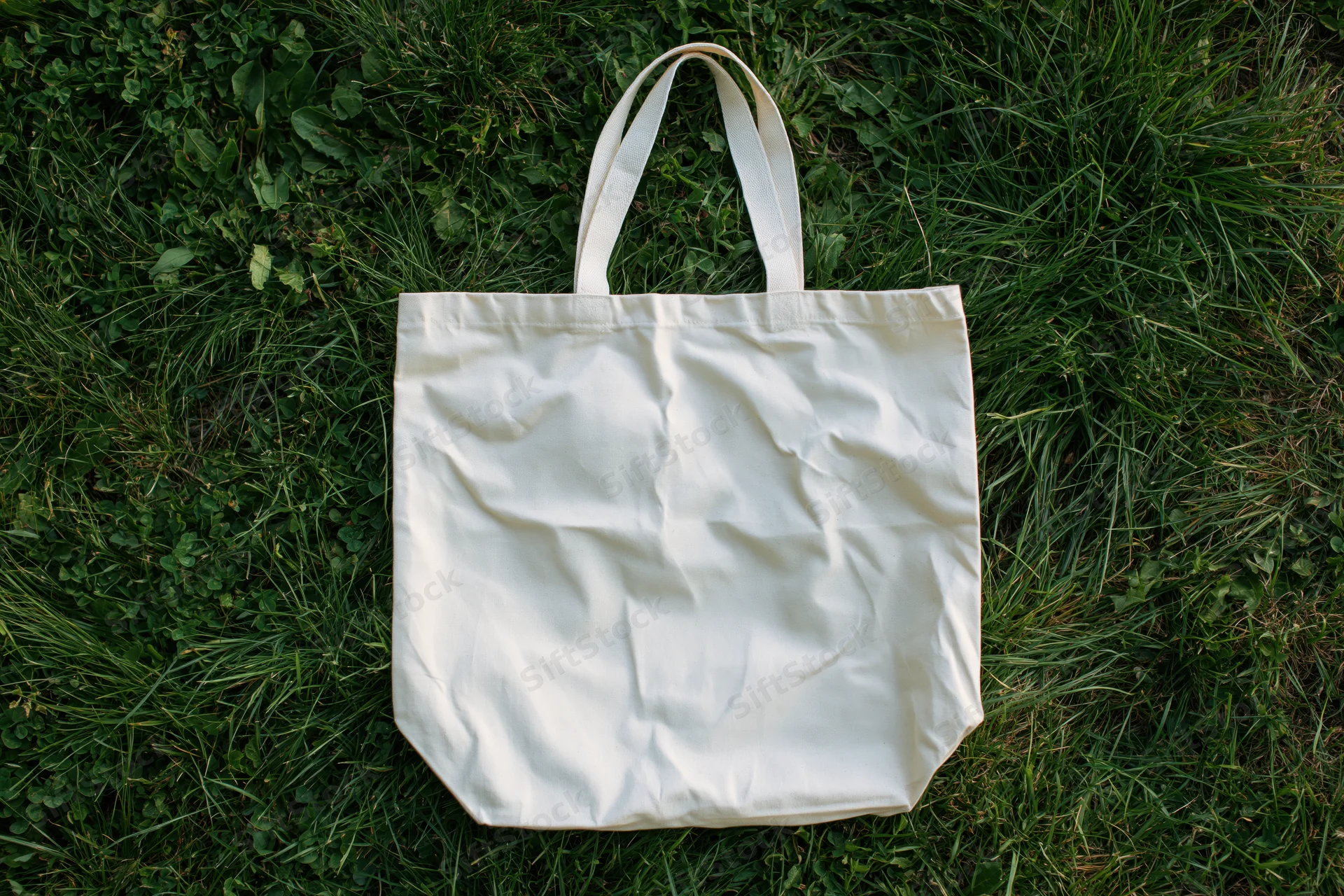 Off-white canvas tote bag lying flat on thick green grass
