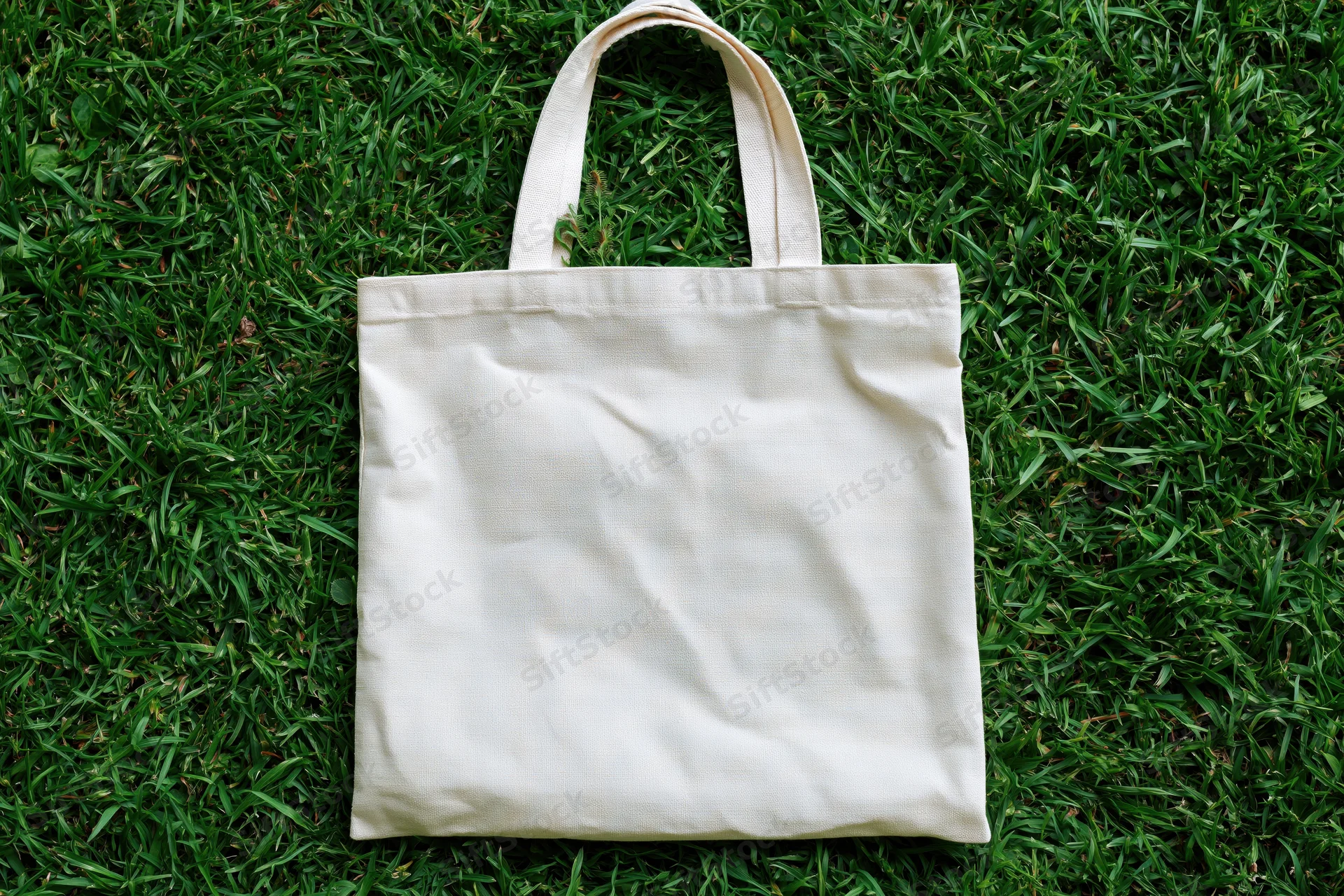 Off-white canvas tote bag lying flat on green grass outdoors