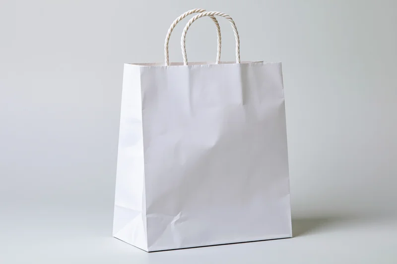 White paper shopping bag with twisted rope handles on a plain light surface
