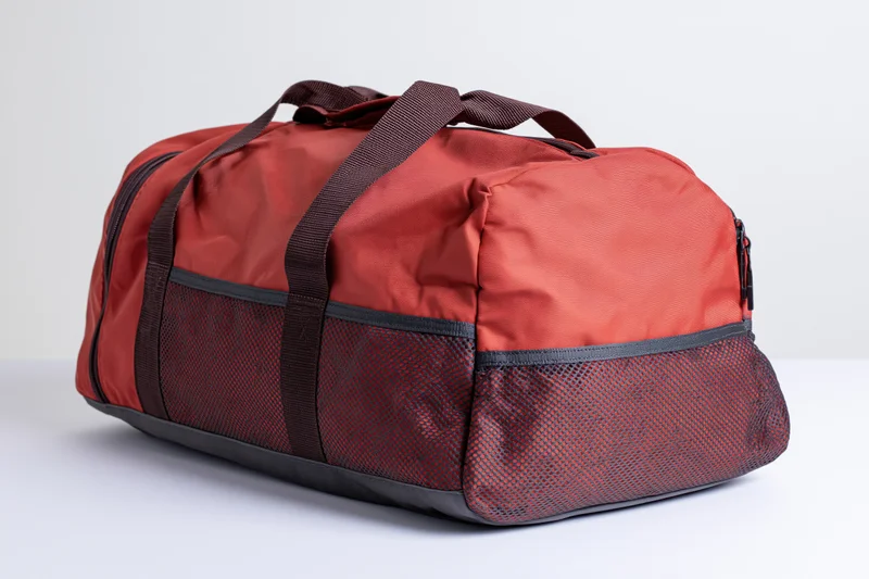 Red and dark grey sports duffel bag with mesh pockets and straps on white surface