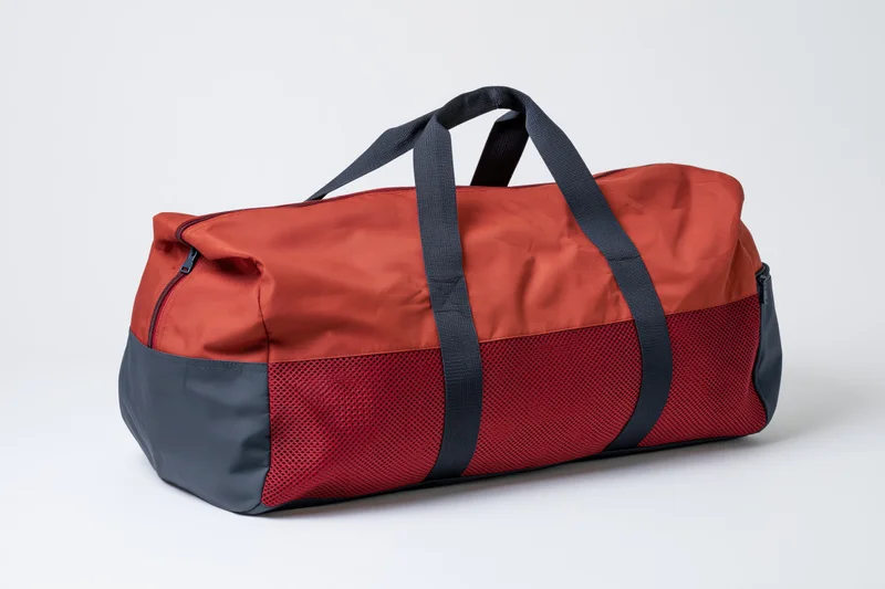 Red and dark grey sports duffel bag with mesh panel and black straps on white background