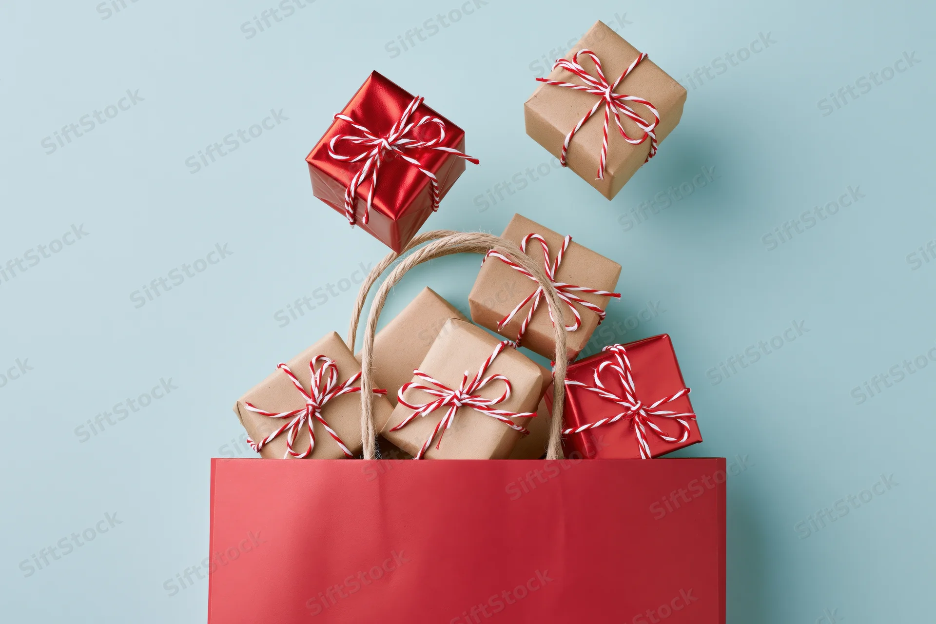 Red shopping bag filled with wrapped gift boxes on light blue surface