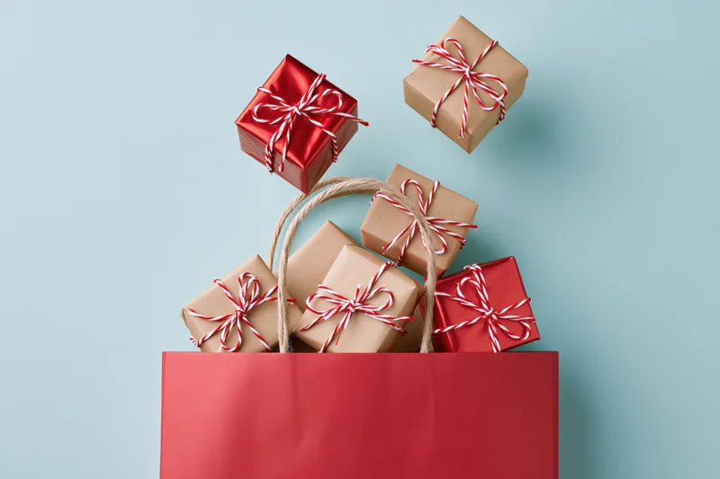 Red shopping bag filled with wrapped gift boxes on light blue surface