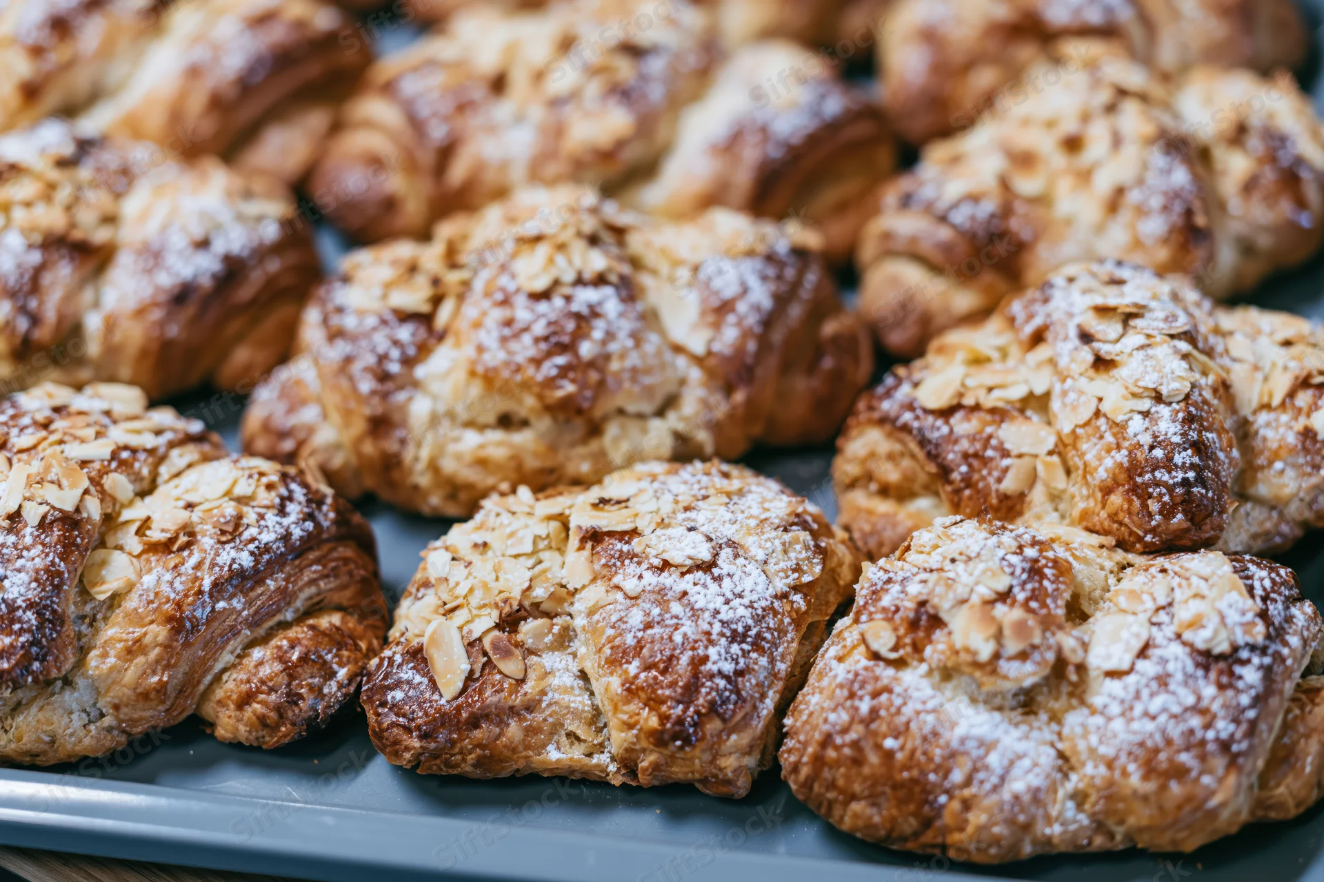 Rows of freshly baked almond croissants arranged tightly on a tray