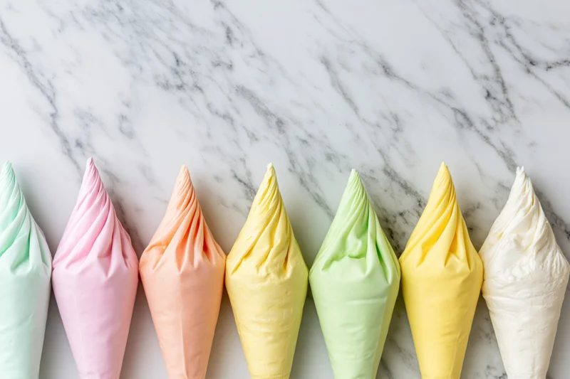 Seven pastel-colored frosting piping bags arranged in a row on a marble countertop