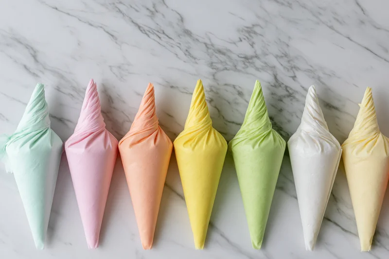 Seven pastel-colored frosting piping bags arranged in a row on a marble surface