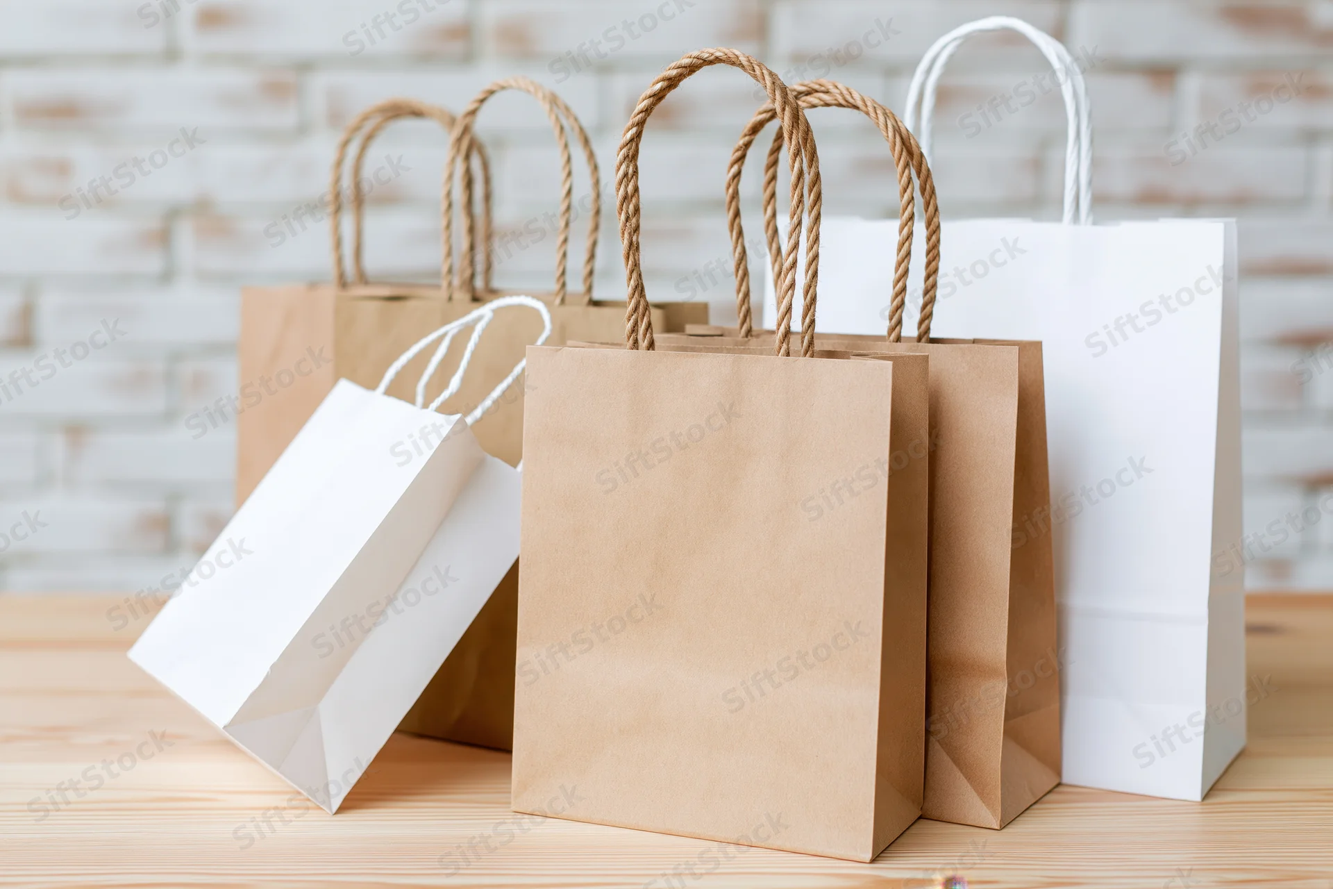 Kraft and white paper shopping bags arranged on a wooden table with copyspace