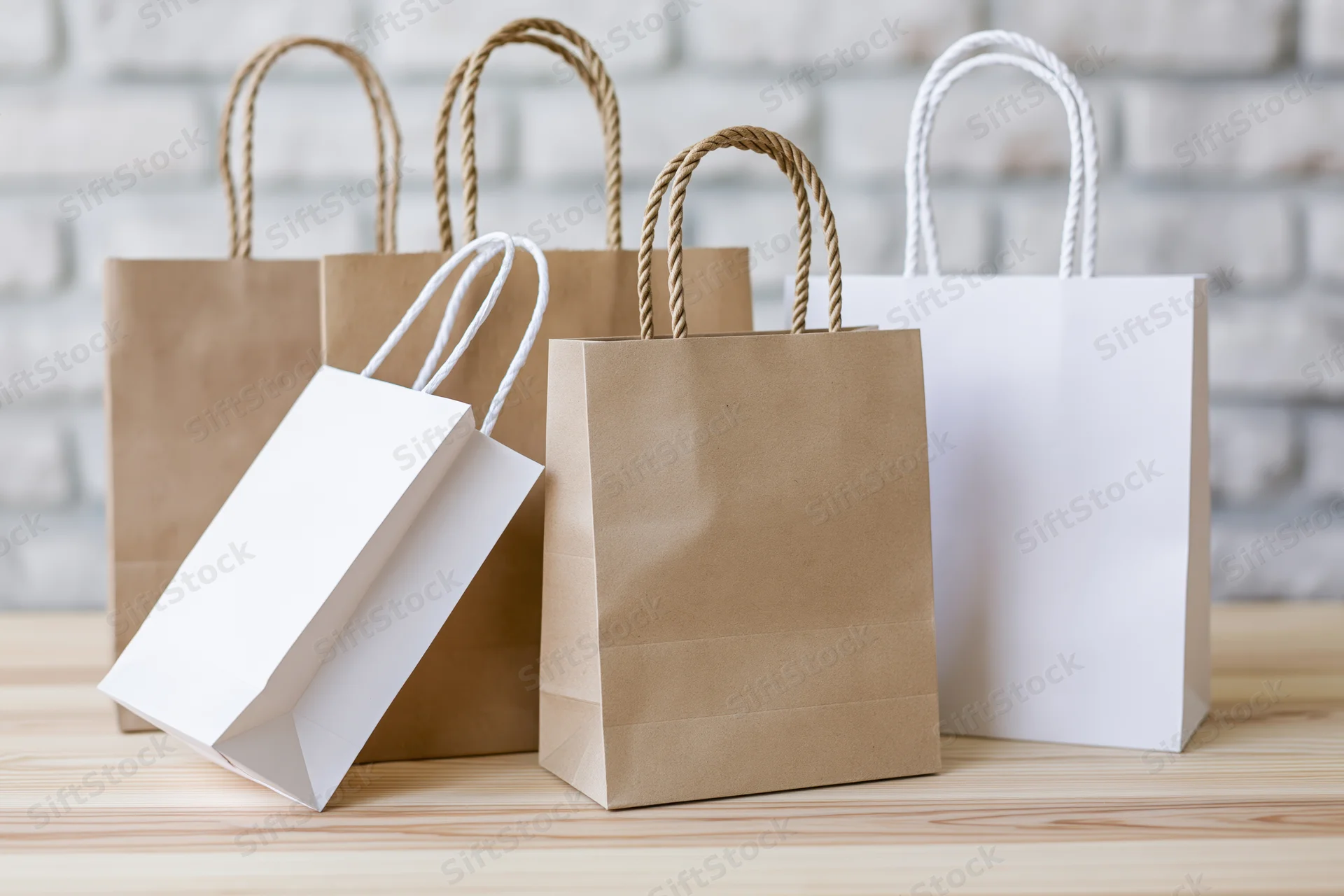 Kraft and white paper shopping bags arranged on a wooden table against a brick wall