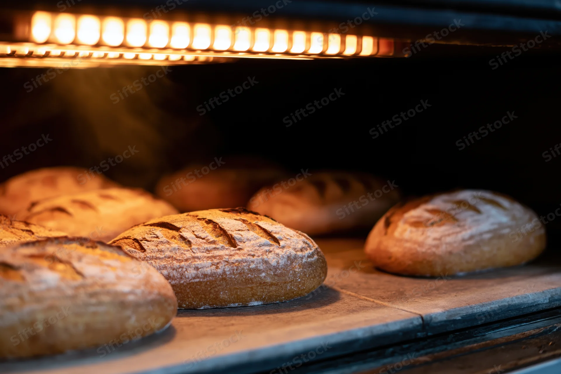 Sourdough loaves baking on a stone deck inside a commercial oven