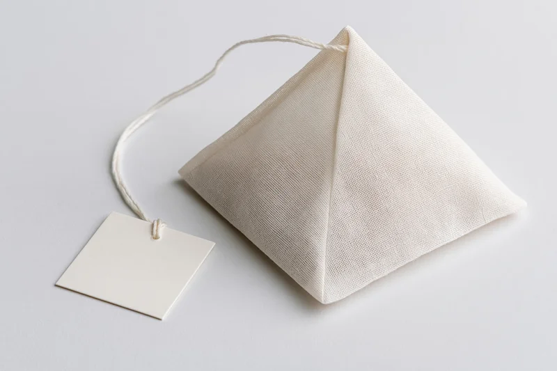 Pyramid-shaped tea bag with white mesh fabric and blank paper tag on white background
