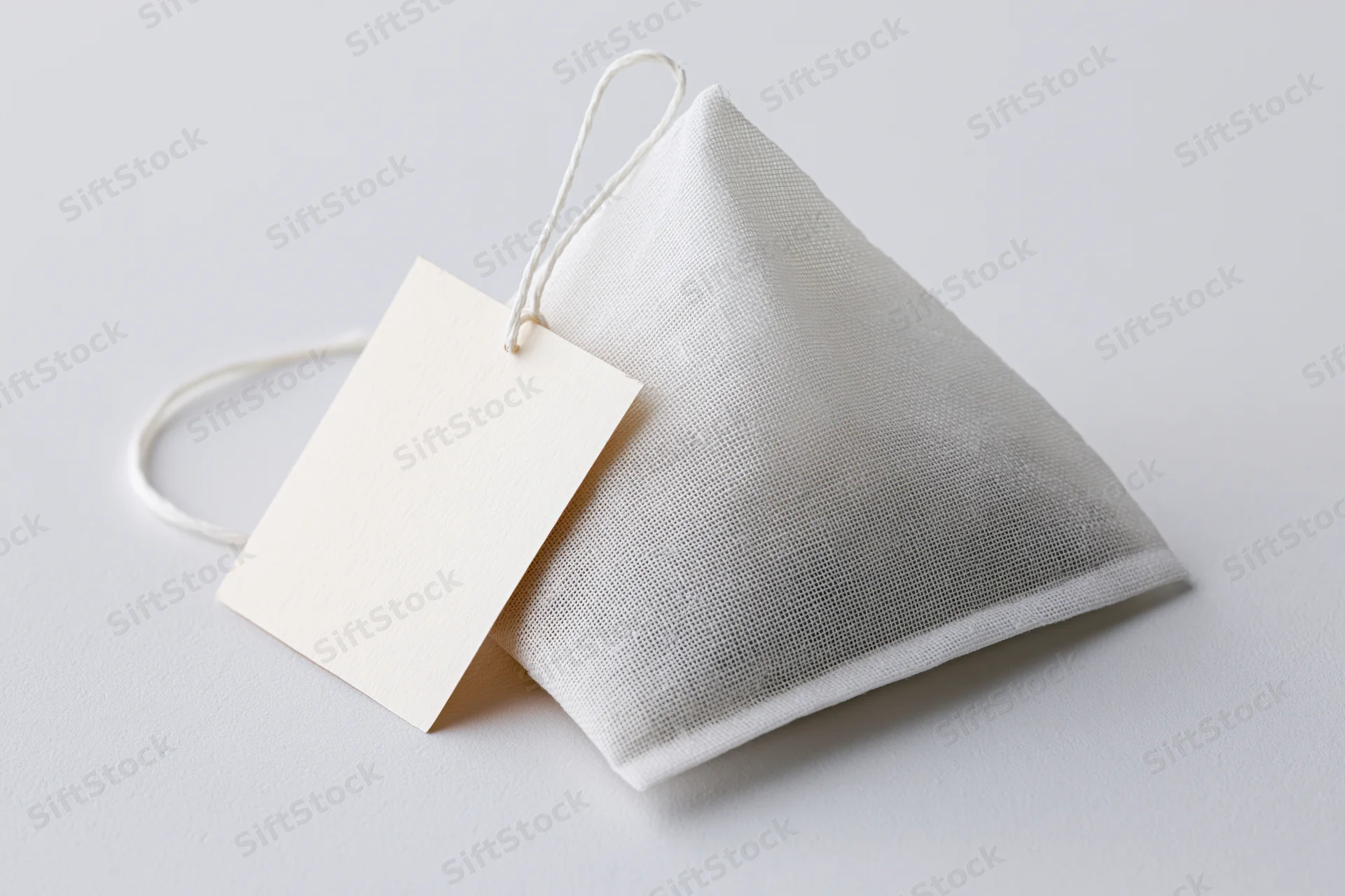 Pyramid-shaped tea bag with white mesh fabric and blank paper tag on white surface