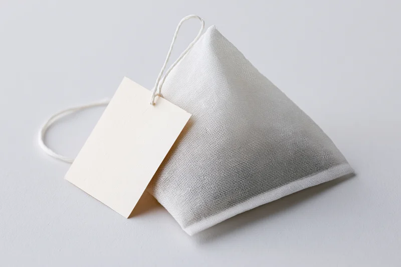 Pyramid-shaped tea bag with white mesh fabric and blank paper tag on white surface