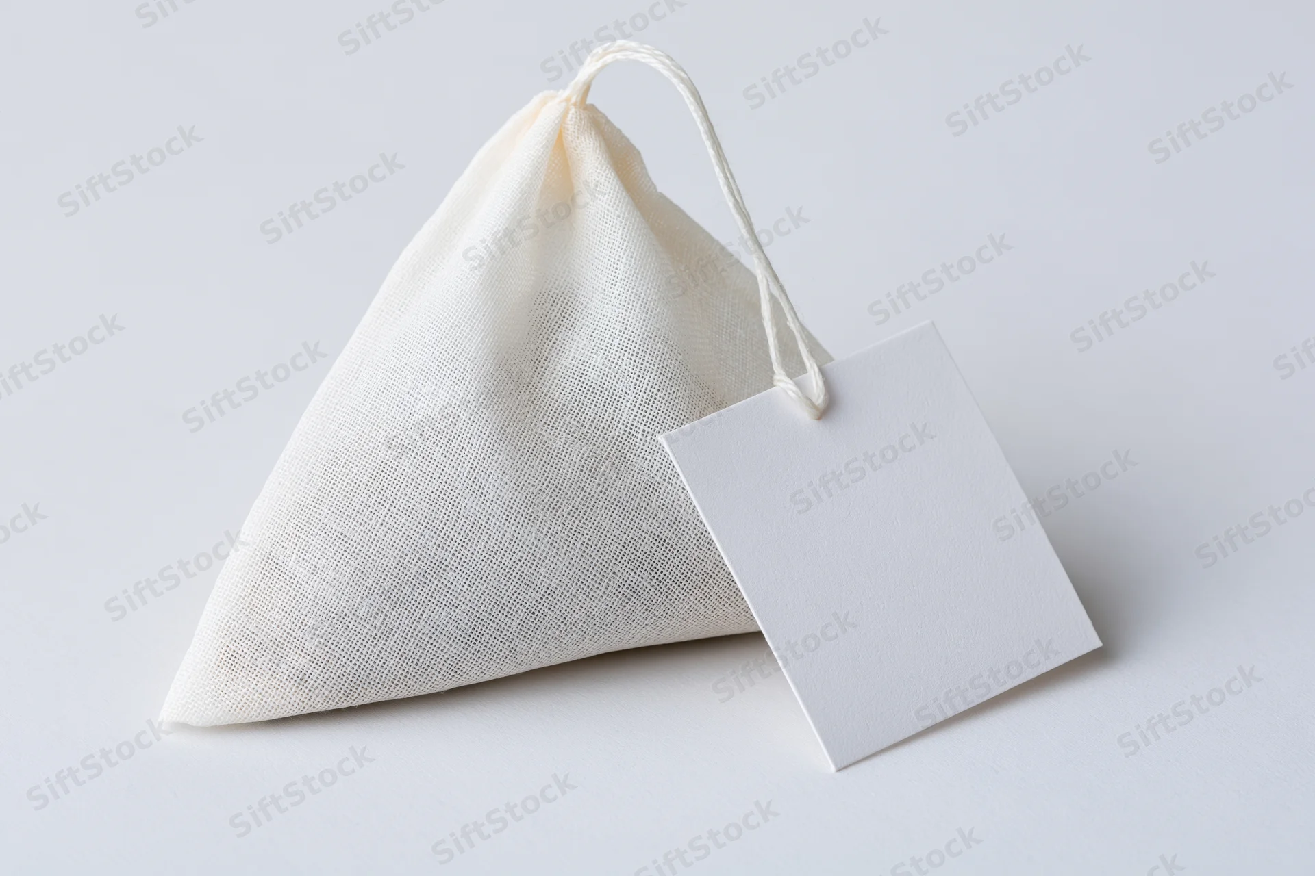 Pyramid-shaped tea bag with white mesh fabric and blank paper tag on white background