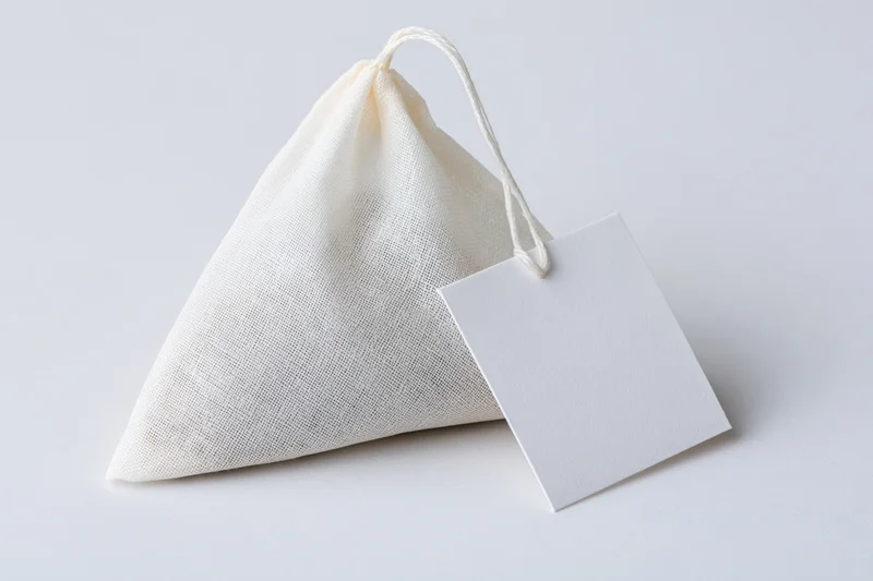 Pyramid-shaped tea bag with white mesh fabric and blank paper tag on white background