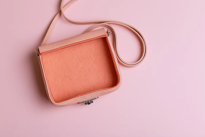 Small blush pink leather crossbody bag with open flap on pink background