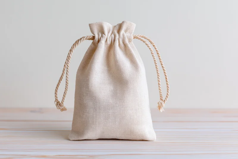 Small natural cotton muslin drawstring pouch sitting upright on wooden surface