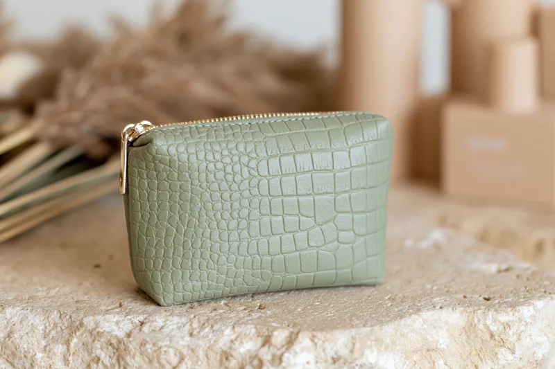 Sage green crocodile-embossed faux leather cosmetic pouch on a stone surface