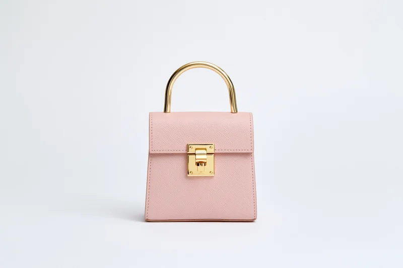 Small structured blush handbag with gold hardware on white background