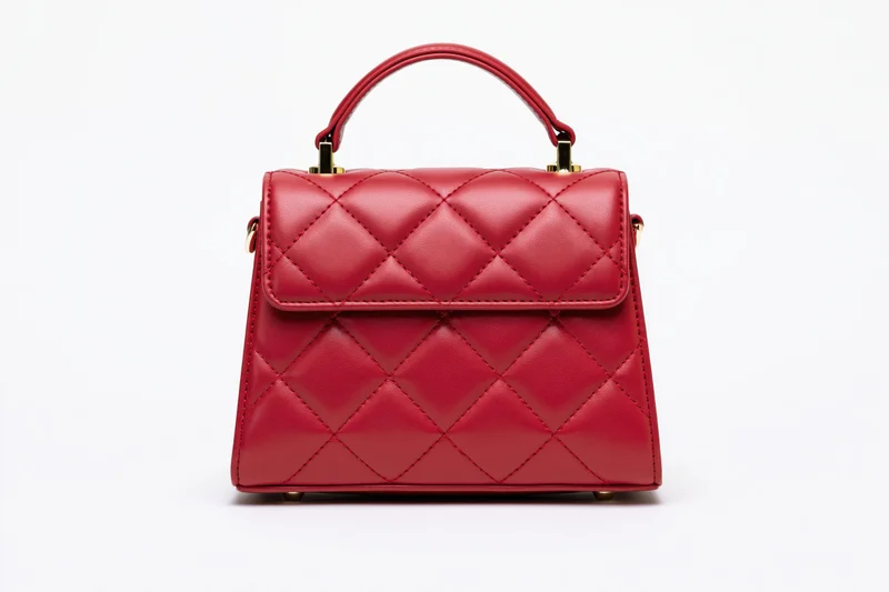 Small structured red leather handbag with quilted diamond stitching and gold hardware on white background