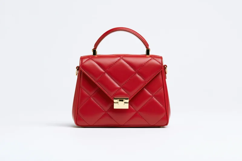 Small red quilted leather handbag with gold hardware on white background