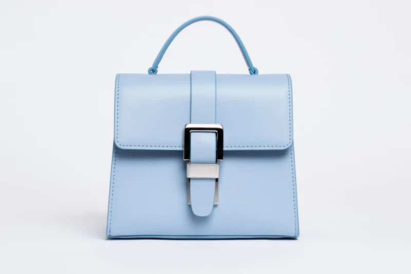 Light blue structured leather handbag with top handle and metallic buckle on white background