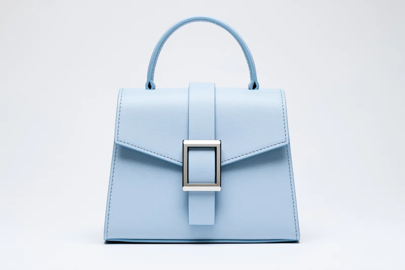 Small structured blue leather handbag with top handle on white background