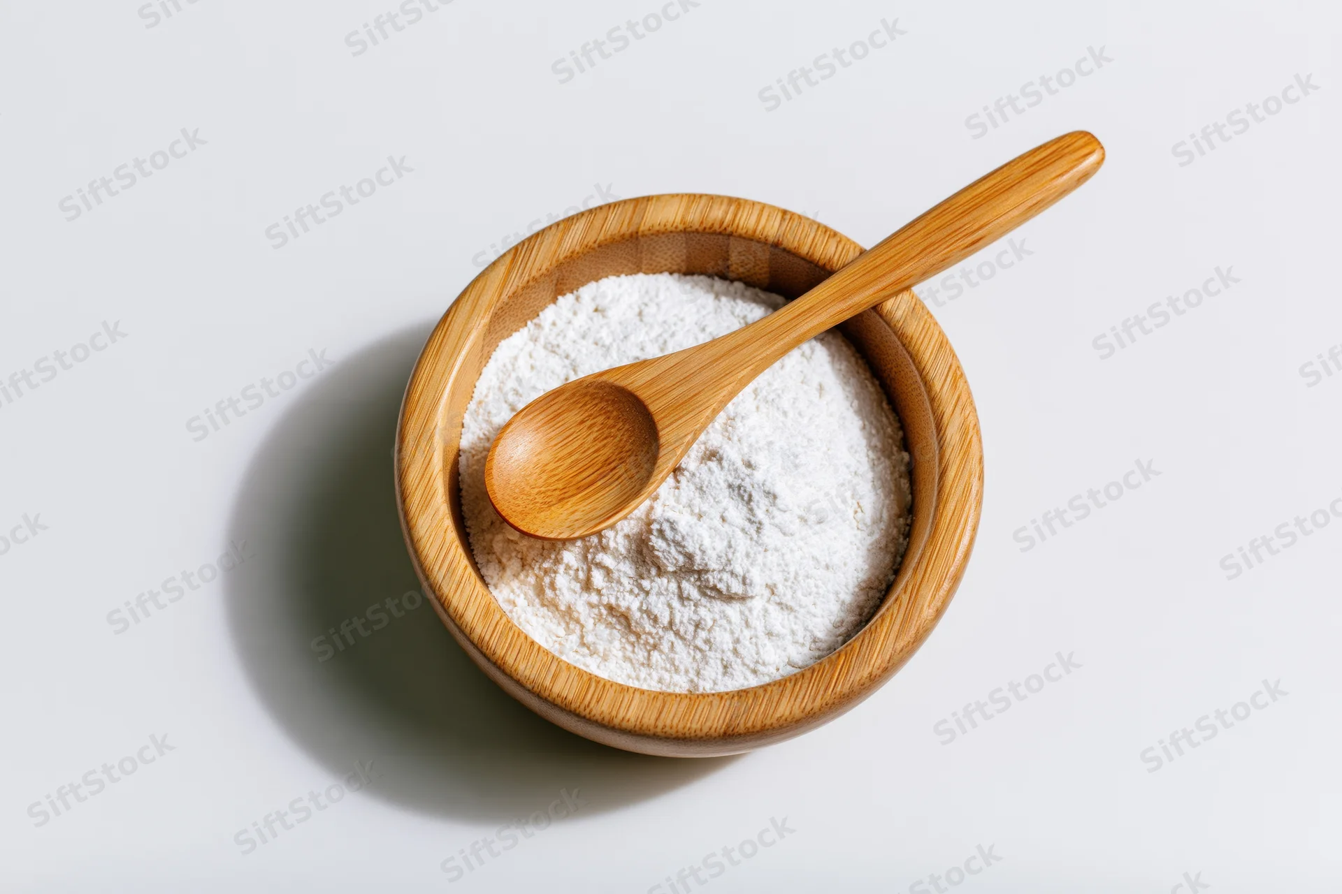 Wooden bowl filled with white flour and a spoon on a plain surface