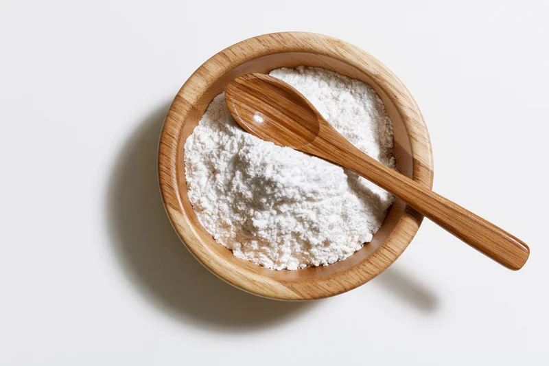 Wooden bowl filled with white flour and a spoon on a plain surface