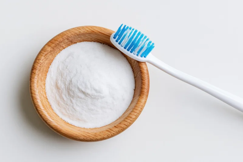 Toothbrush resting on a wooden bowl filled with white baking soda powder on a plain white surface