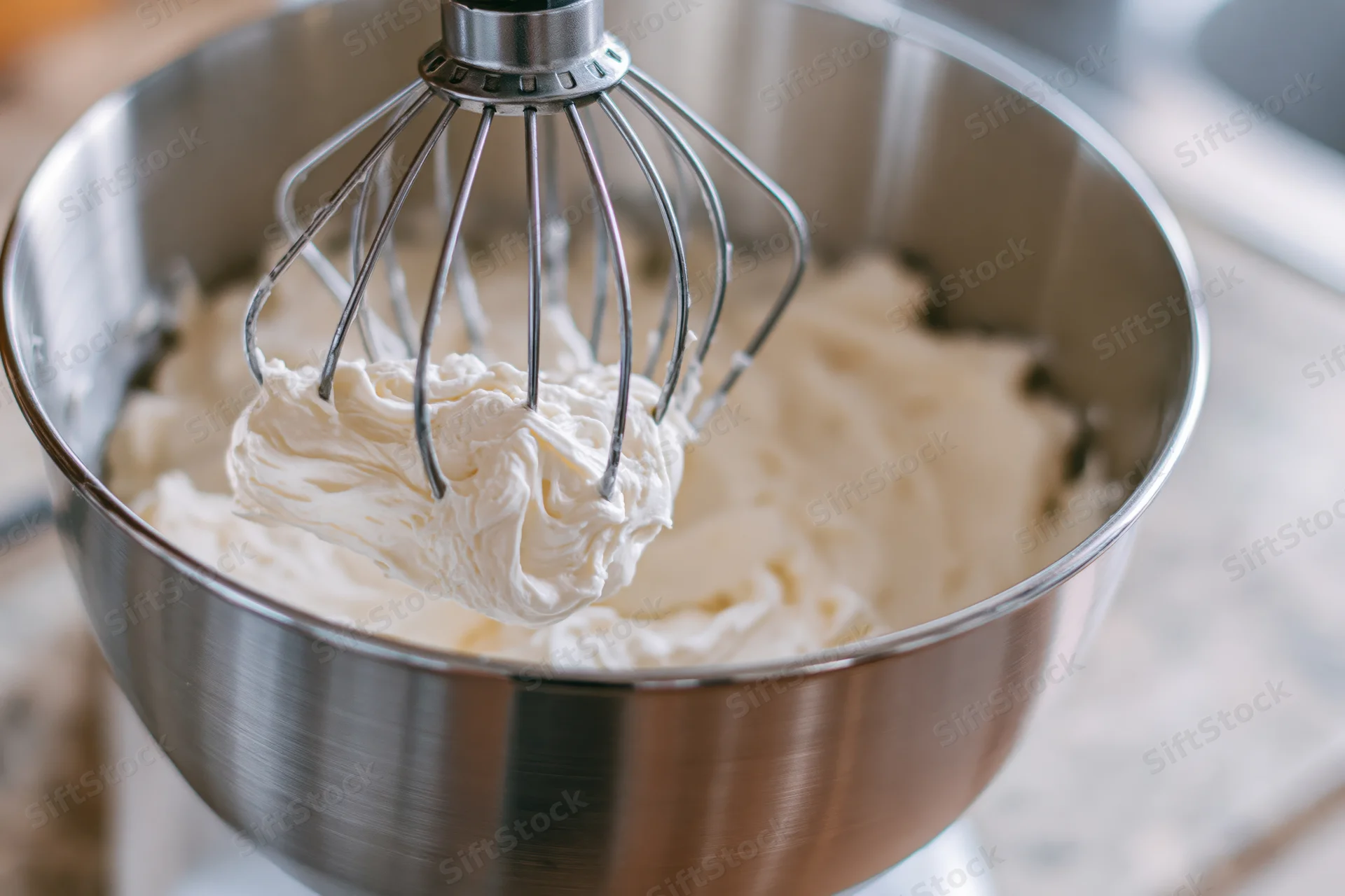 Whisk attachment lifting thick white cream from stainless steel bowl in kitchen