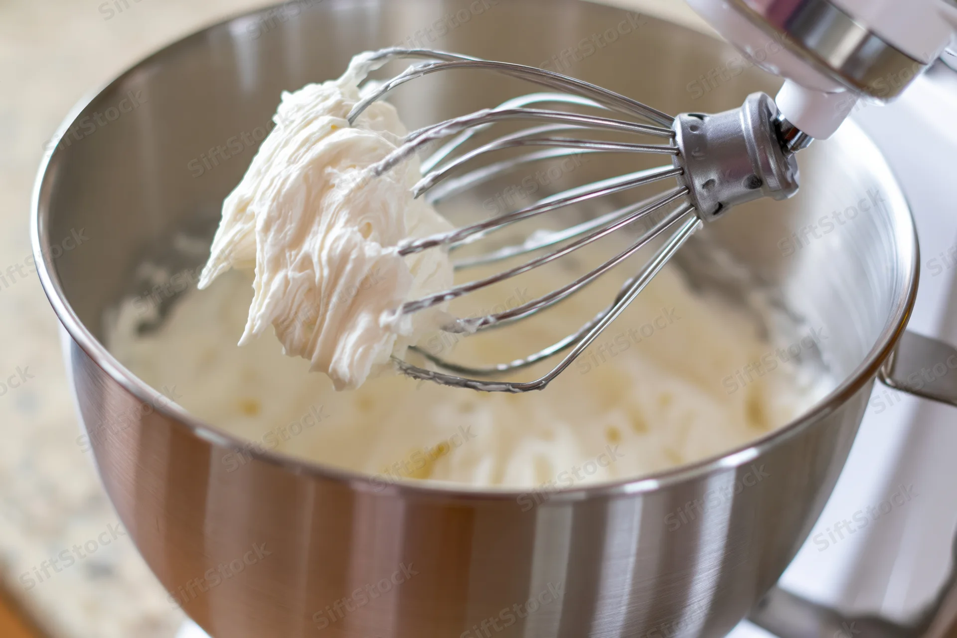 Whisk attachment lifting thick white cream from stainless steel bowl in kitchen