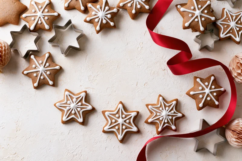 Star-shaped gingerbread cookies with white icing and red ribbon arranged on a textured surface with cookie cutters and paper ornaments