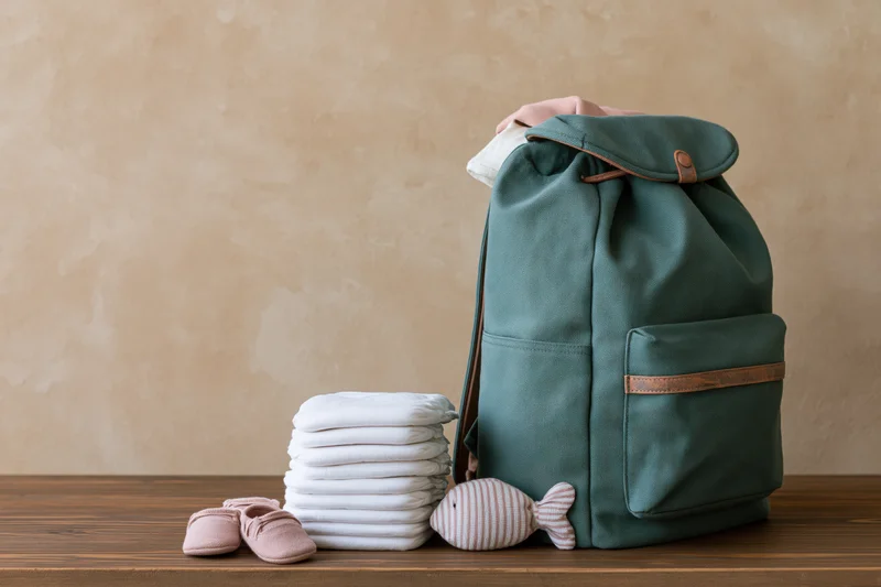 Teal canvas diaper bag backpack with baby essentials on wooden surface
