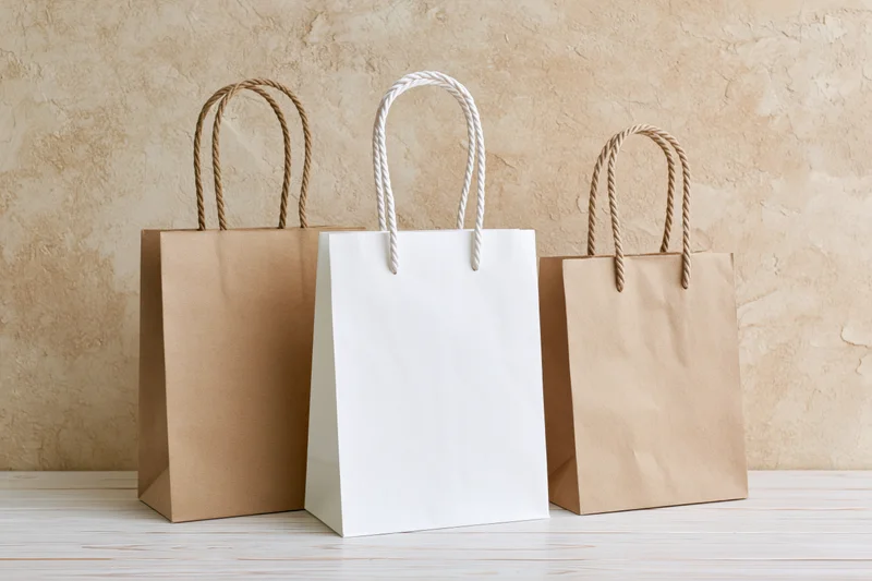 Three plain paper shopping bags arranged on a white wooden surface