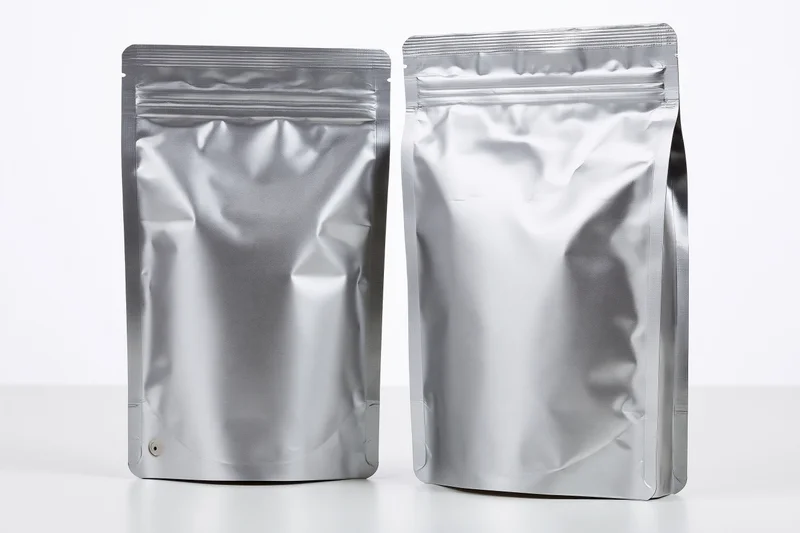 Two blank matte silver foil coffee bags standing upright side by side on white surface
