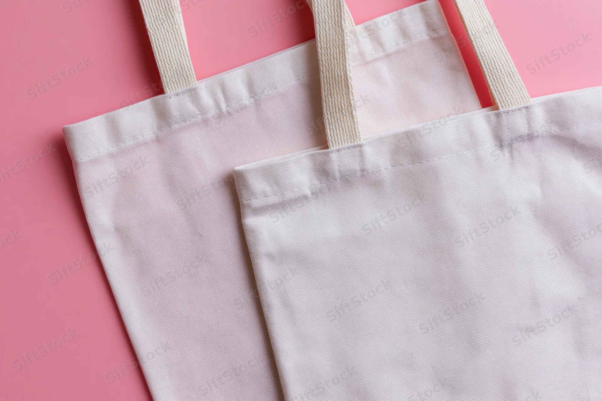 Two blank white canvas tote bags with woven cotton handles on pink background