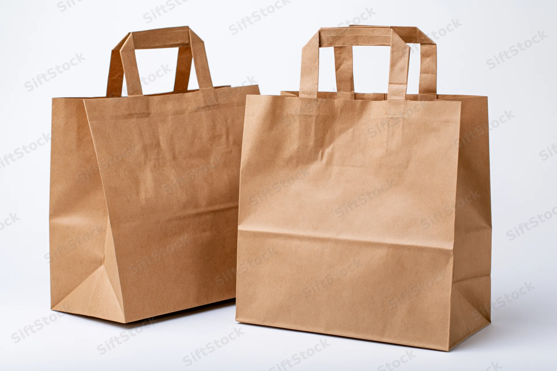 Two brown kraft paper shopping bags with flat handles standing side by side on white surface