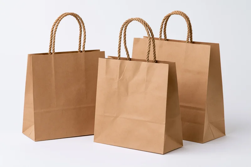 Three brown kraft paper shopping bags with twisted rope handles arranged on a white surface