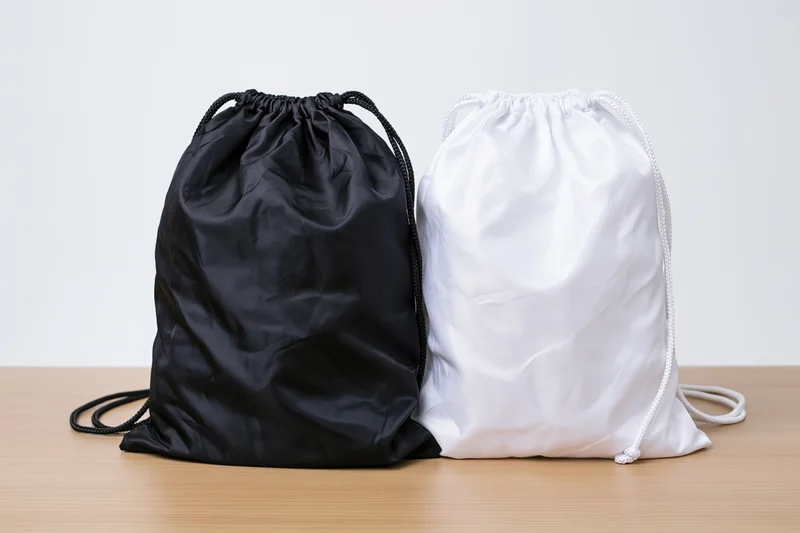Two drawstring backpacks in black and white placed side by side on a wooden surface against a plain white background