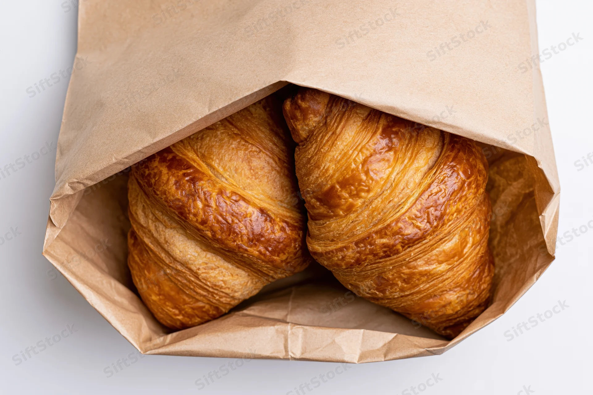 Two golden-brown croissants in an open kraft paper bag