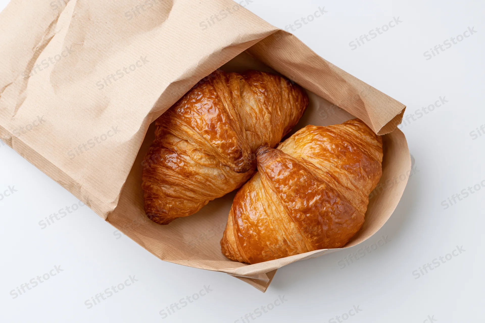 Two golden-brown croissants in an open kraft paper bag on white background