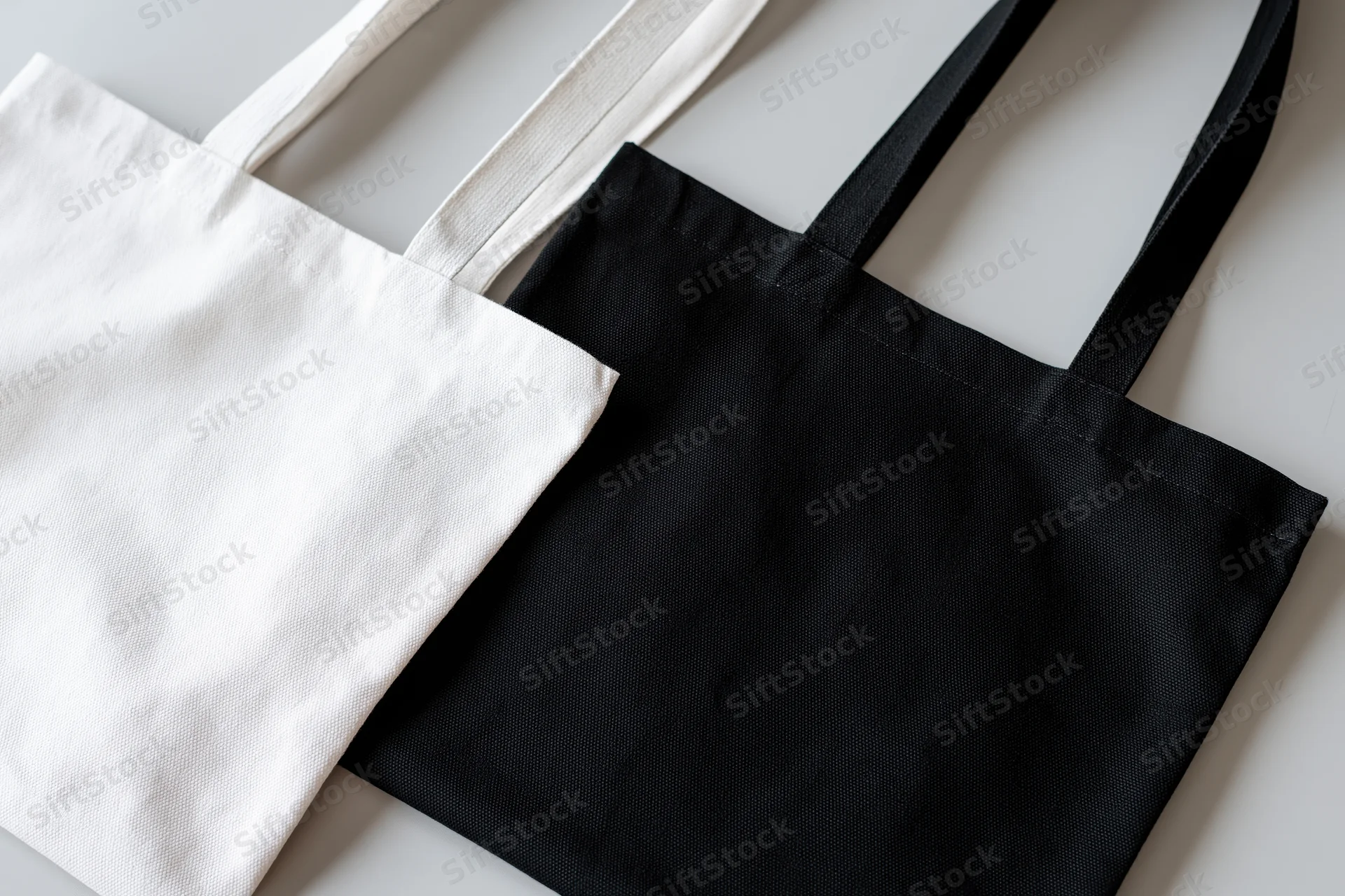 Two plain canvas tote bags in white and black laid flat on a light surface