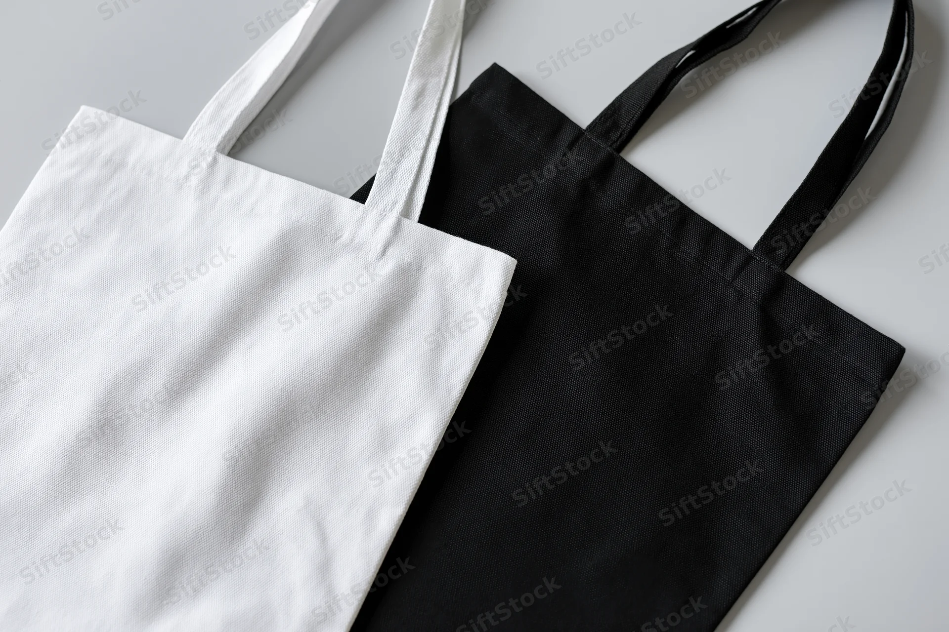 Two plain canvas tote bags one white and one black laid flat on a light surface