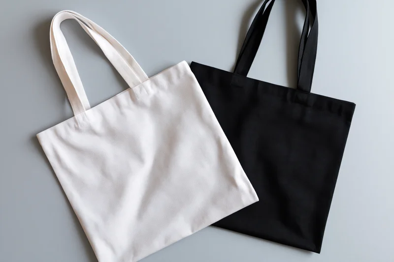Two plain canvas tote bags laid flat on a gray surface