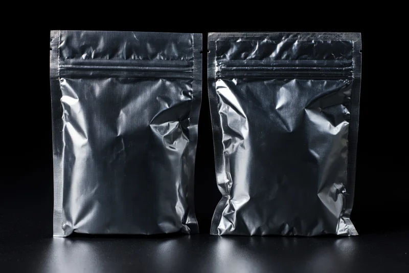 Two sealed metallic foil snack pouches standing side by side on a dark surface