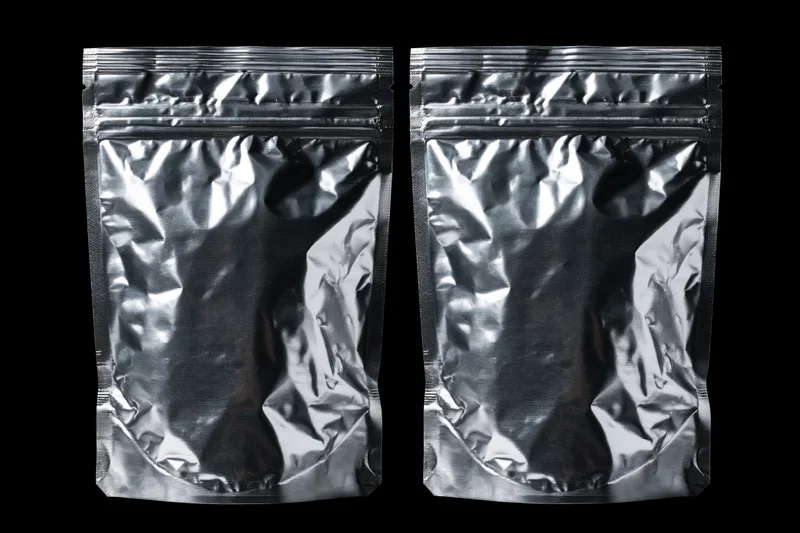 Two sealed metallic foil snack pouches side by side on black background