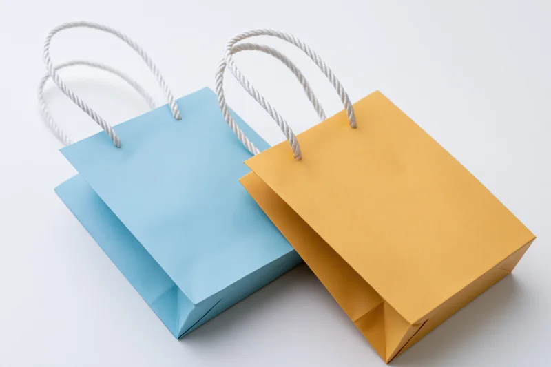 Two small paper shopping bags one light blue and one mustard on white background